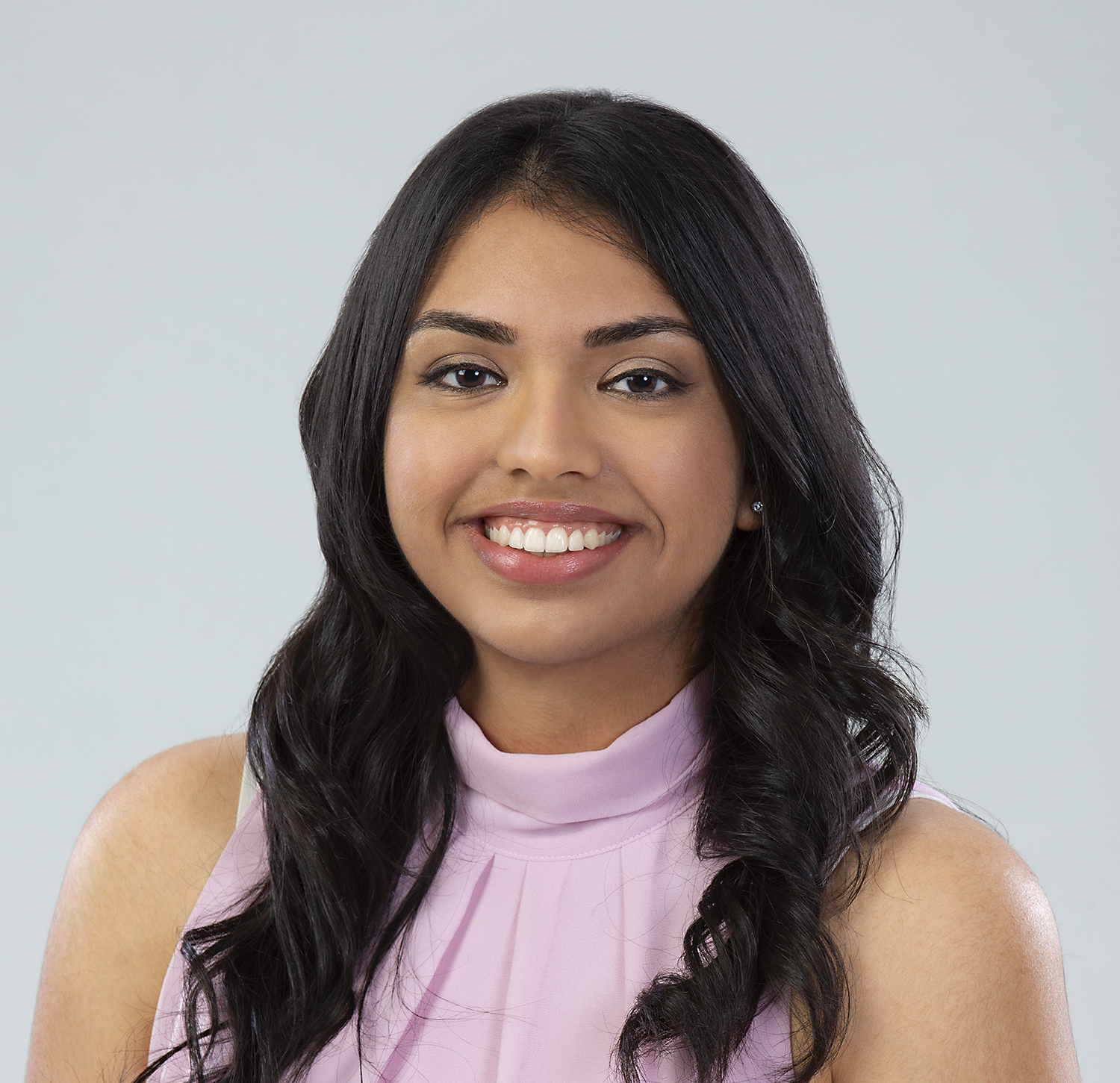 A headshot of Jesmeen Kaur Deo, wearing a black blouse and smile in front of a dark green background.